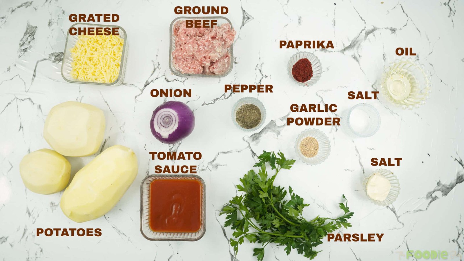 Ingredients for cheesy beef potato balls laid out on a counter, including potatoes, ground beef, onion, parsley, tomato sauce, spices, oil, and grated cheese