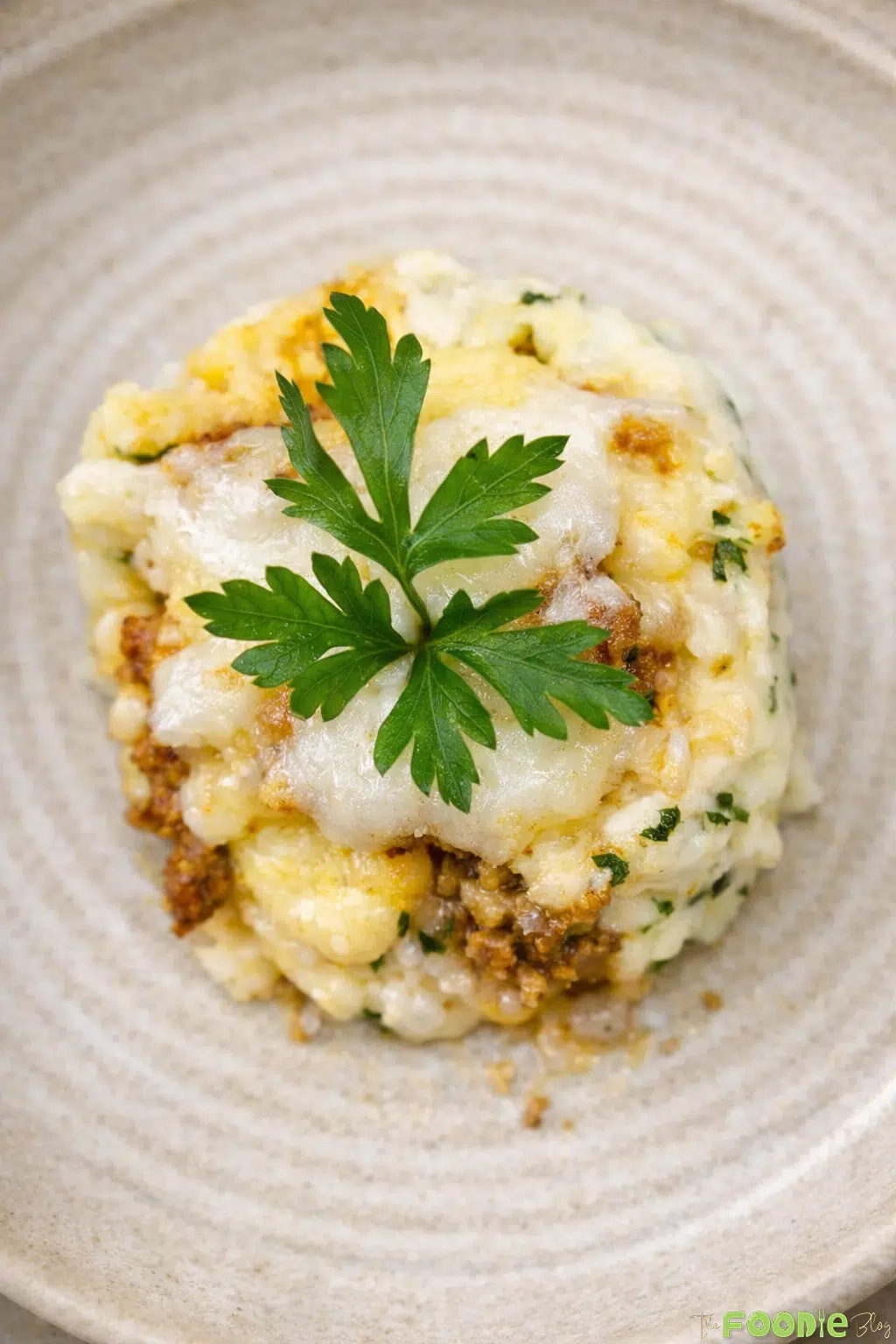 Plated cheesy beef potato balls topped with melted cheese and parsley garnish.