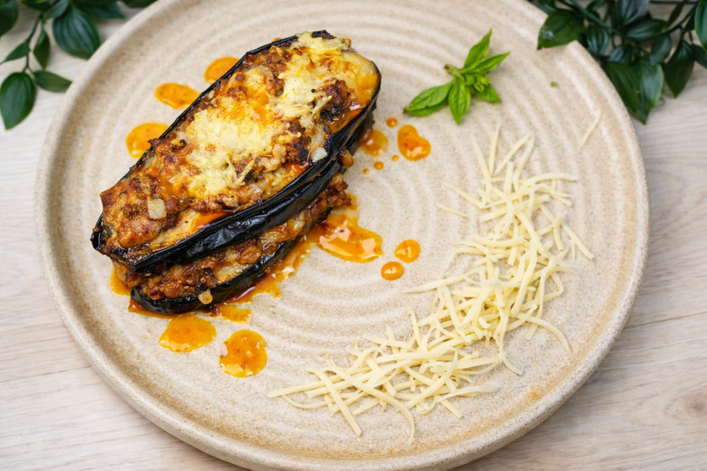 Plated cheesy beef-stuffed eggplant boats topped with melted mozzarella and served with extra shredded cheese.