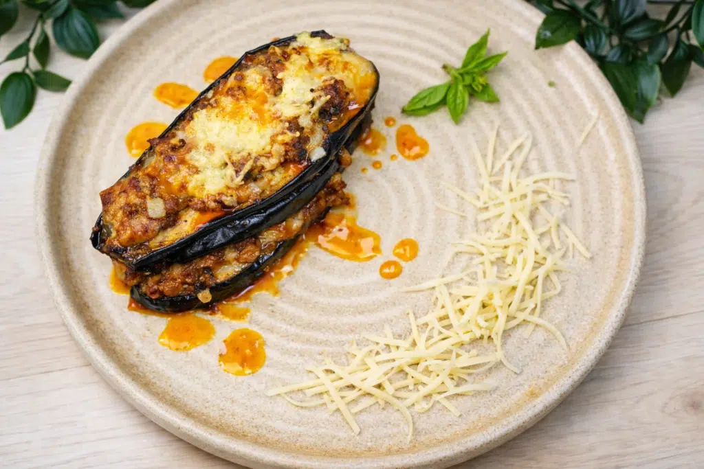 Plated cheesy beef-stuffed eggplant boats topped with melted mozzarella and served with extra shredded cheese.