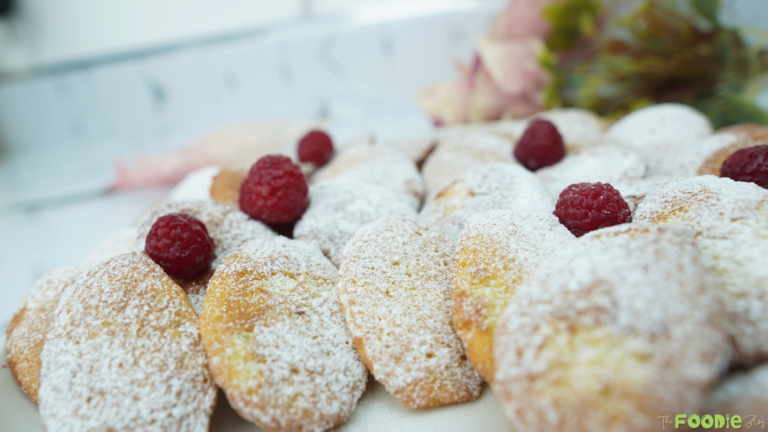 Plate of classic madeleines covered in powdered sugar with raspberries on top