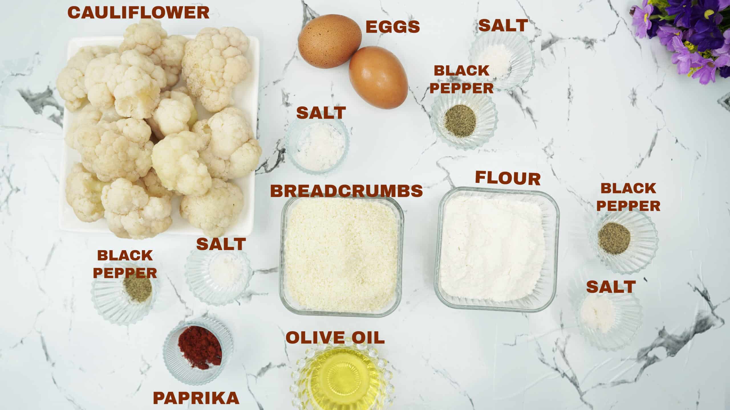 Cauliflower, breadcrumbs, flour, eggs, olive oil, and spices measured out on a counter