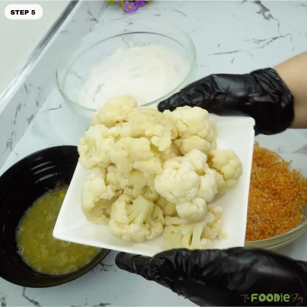 Par-cooked cauliflower florets on a plate next to breading bowls