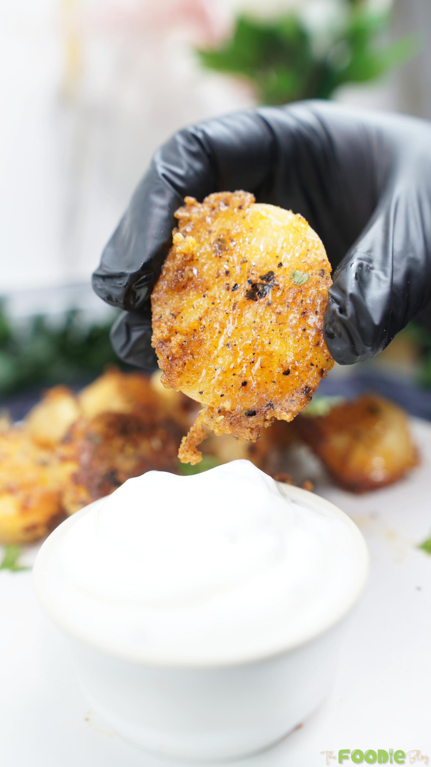 A gloved hand dipping a crispy Parmesan potato into a bowl of sour cream dip