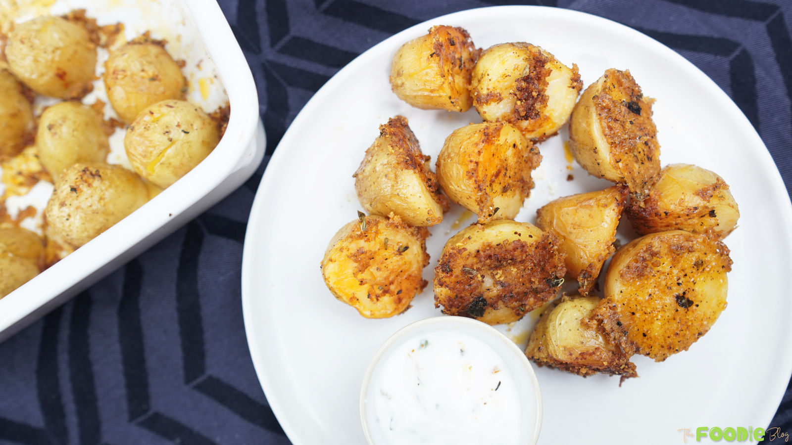 Crispy Parmesan baby potatoes with a golden crust served with sour cream dip on a white plate