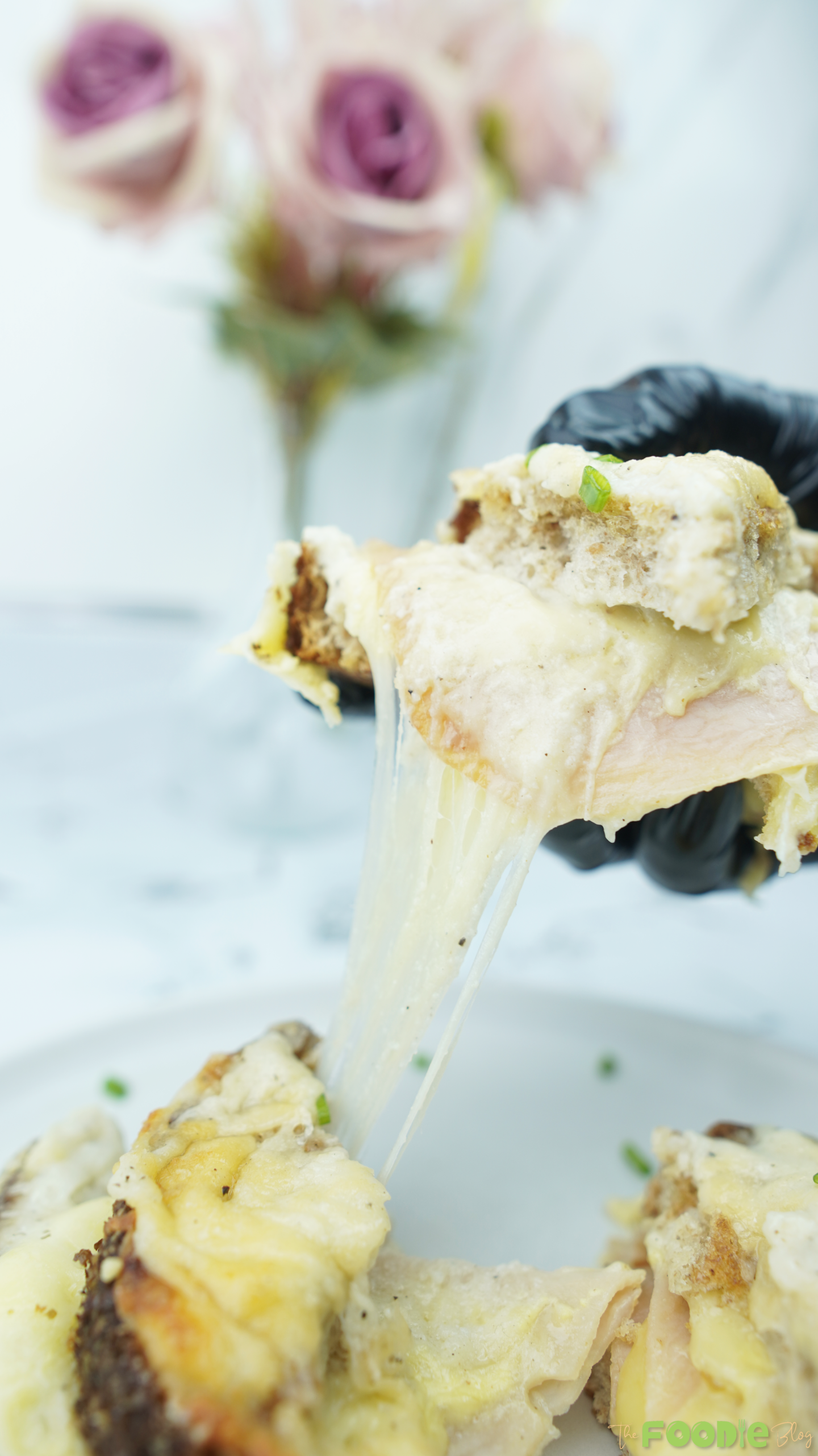 A hand lifting a gooey bite of ham and cheese sandwich with béchamel sauce stretching