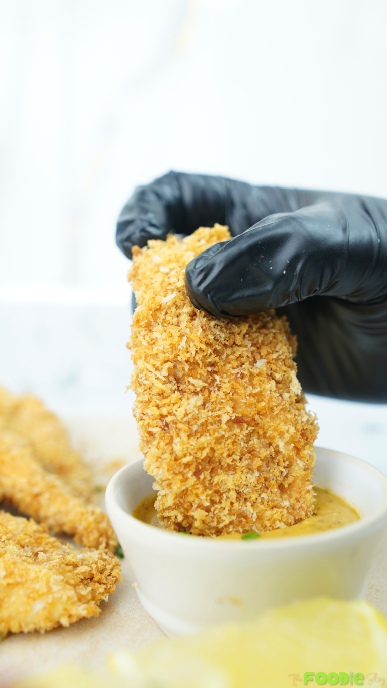 Hand holding a crispy baked chicken tender dipped into a creamy sauce