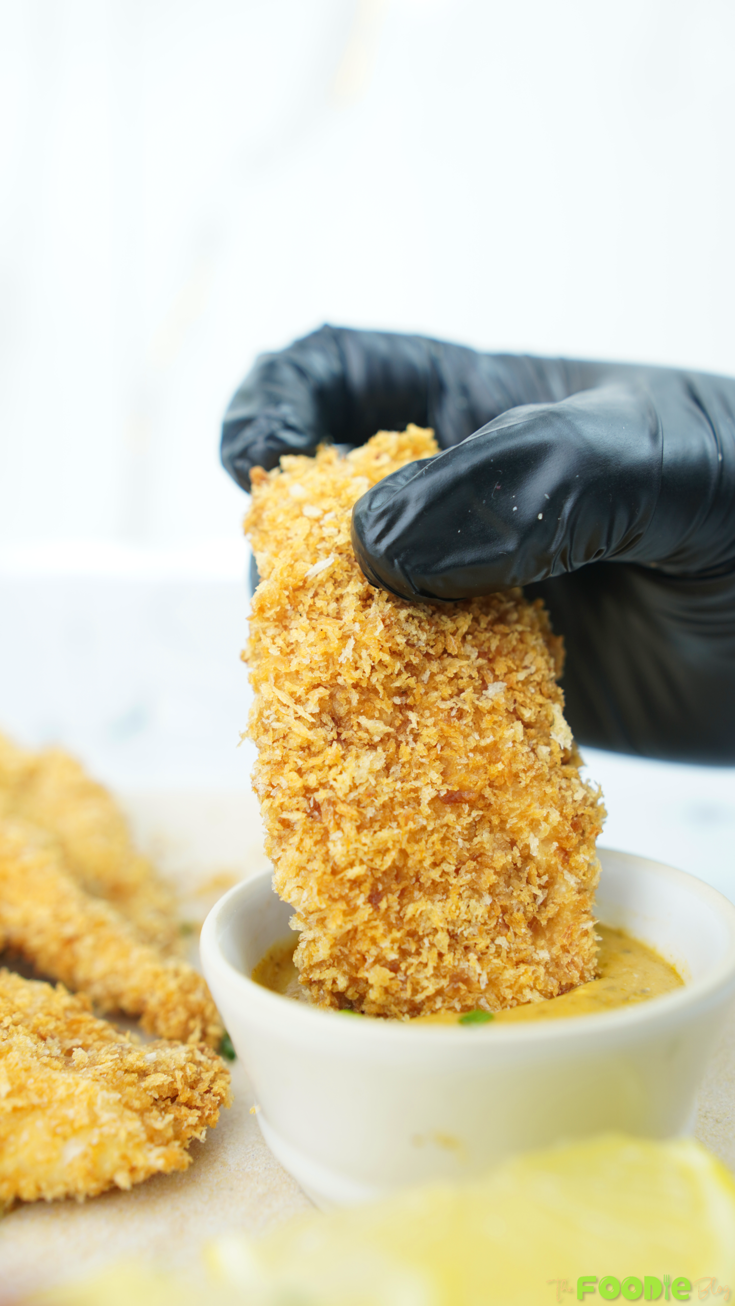 Hand holding a crispy baked chicken tender dipped into a creamy sauce