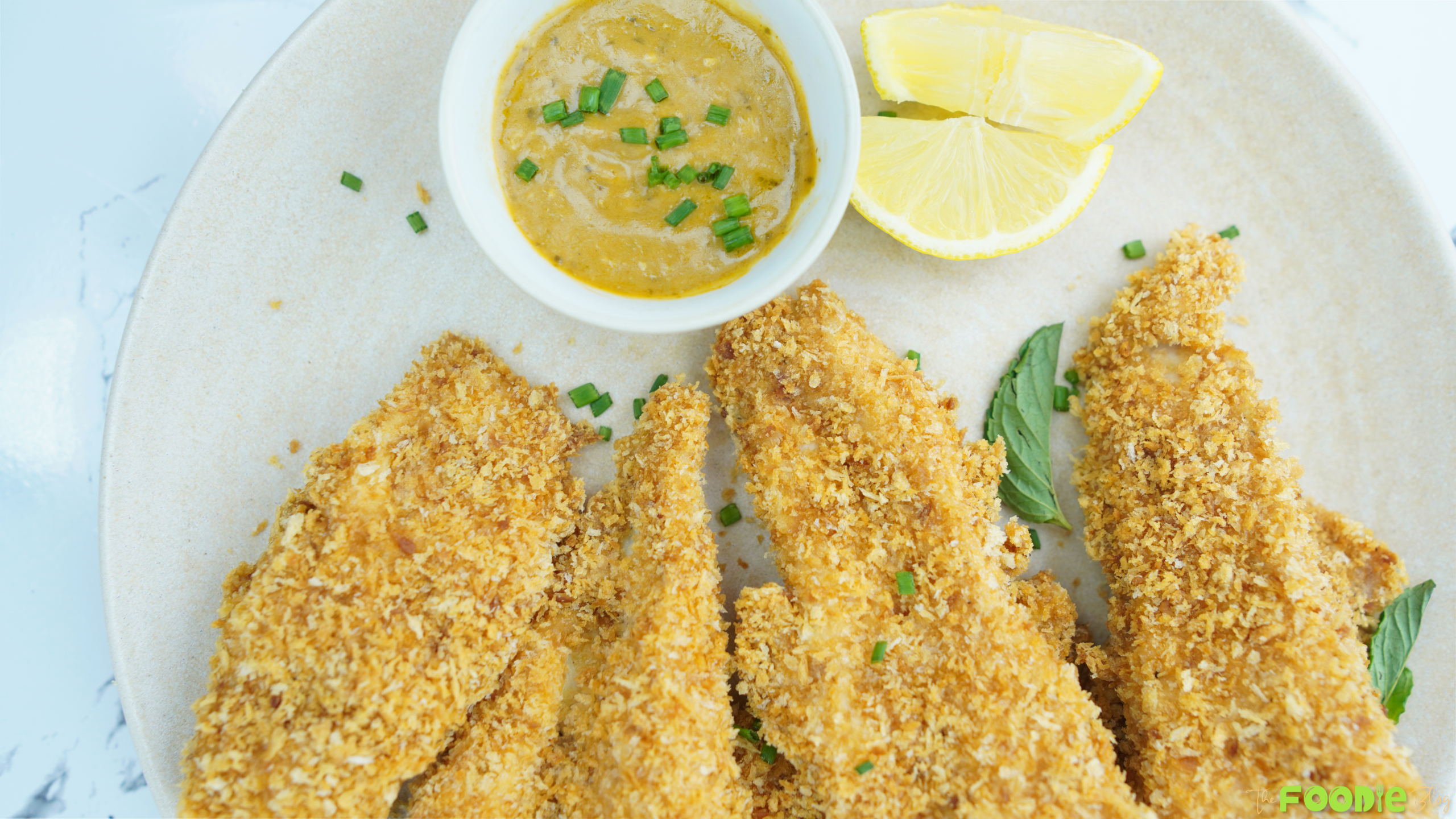 Crispy baked chicken tenders with dipping sauce and lemon wedges on a plate