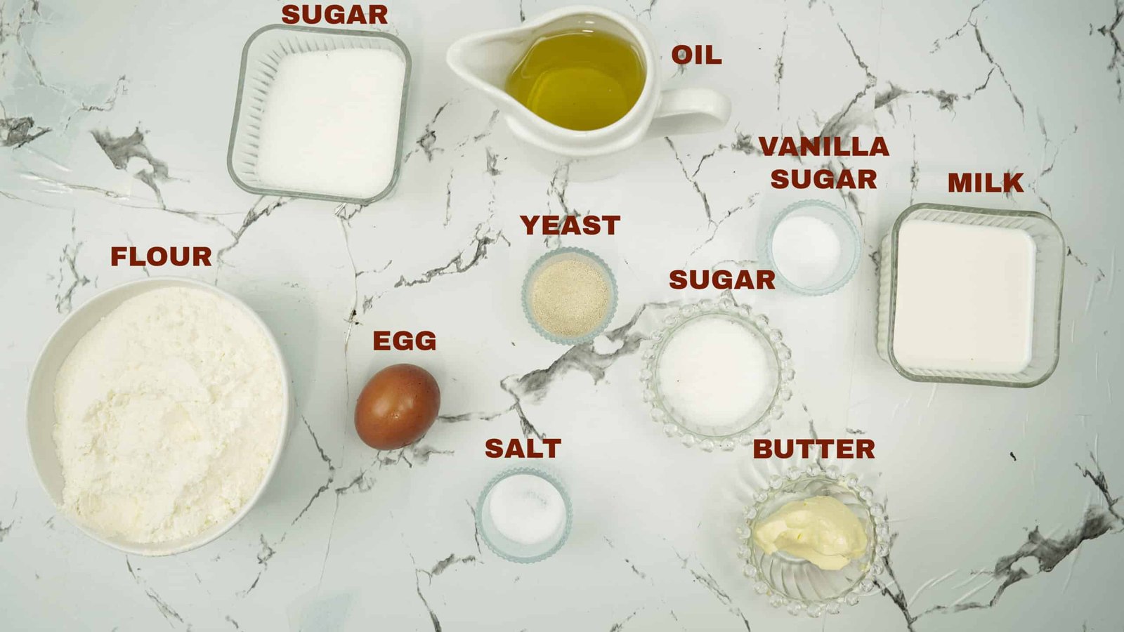 Flour, milk, sugar, yeast, egg, butter, oil, and salt arranged on a counter