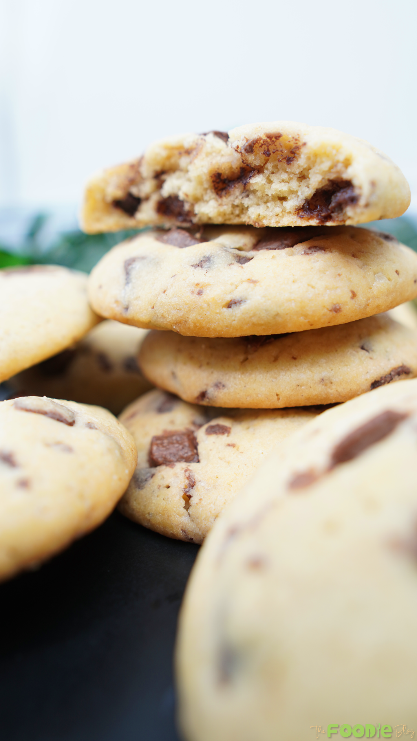 Broken chocolate chip cookies stacked with crumbs on a dark surface