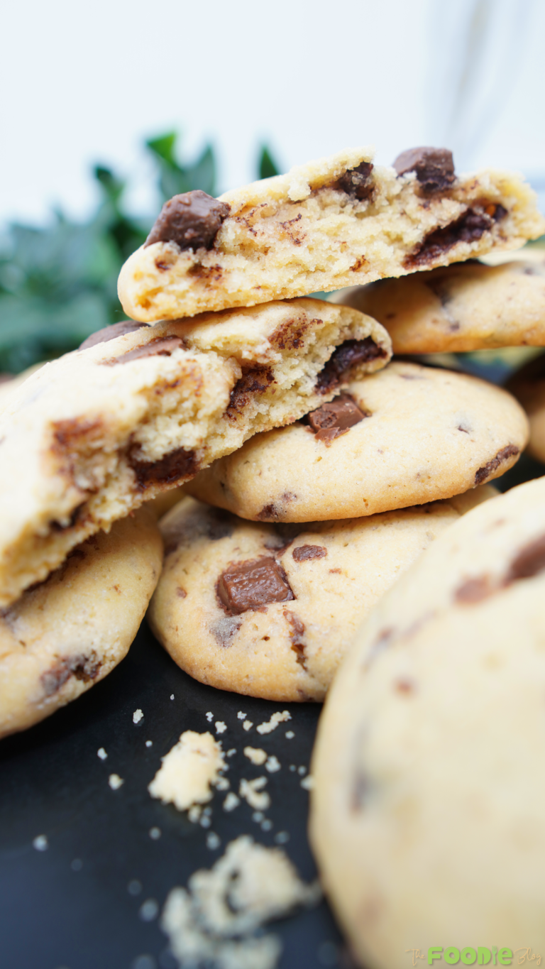Chocolate chip cookies piled on a black plate with a yellow cloth background