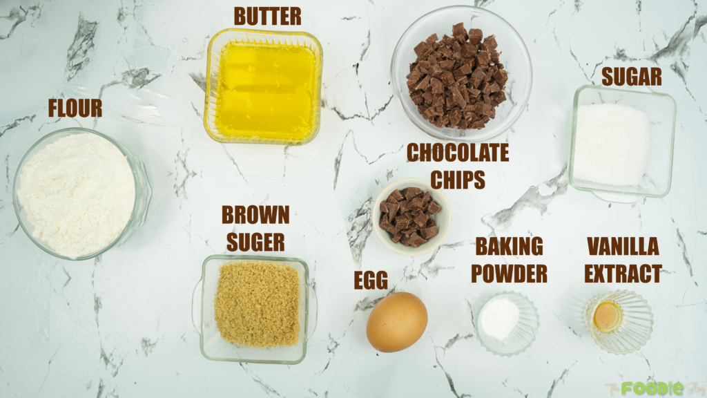 Bowls of flour, sugars, butter, chocolate chips, egg, baking powder, and vanilla on a marble surface