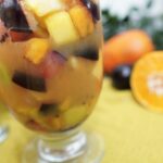Close-up of fruit salad showing pineapple chunks, plum pieces, and kiwi in orange juice