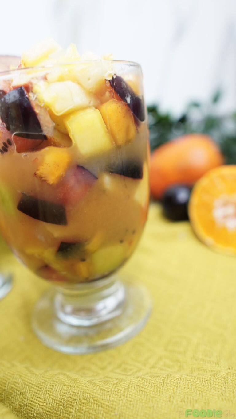 Close-up of fruit salad showing pineapple chunks, plum pieces, and kiwi in orange juice