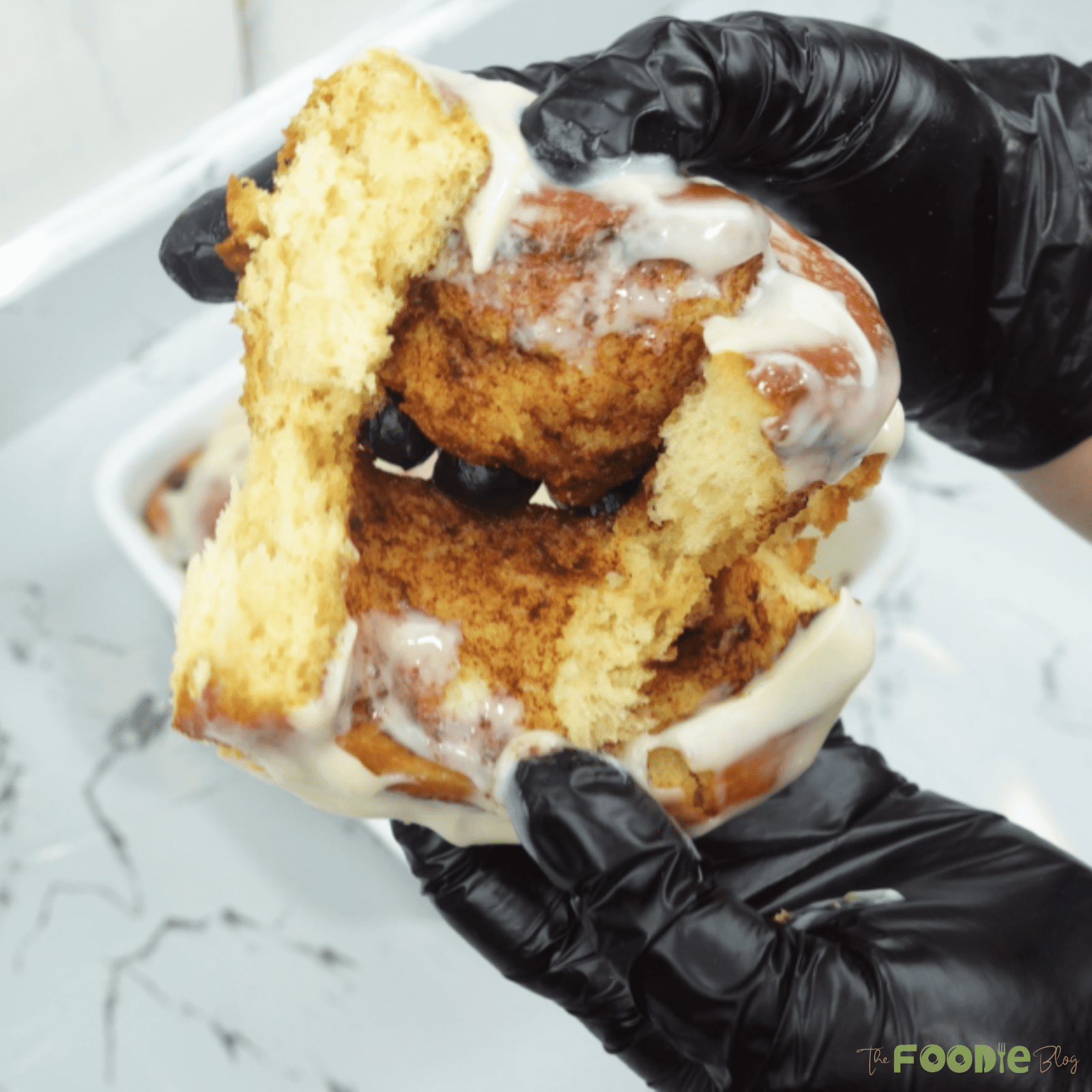 Hands pulling apart a cinnamon roll to show the gooey cinnamon swirl and creamy icing