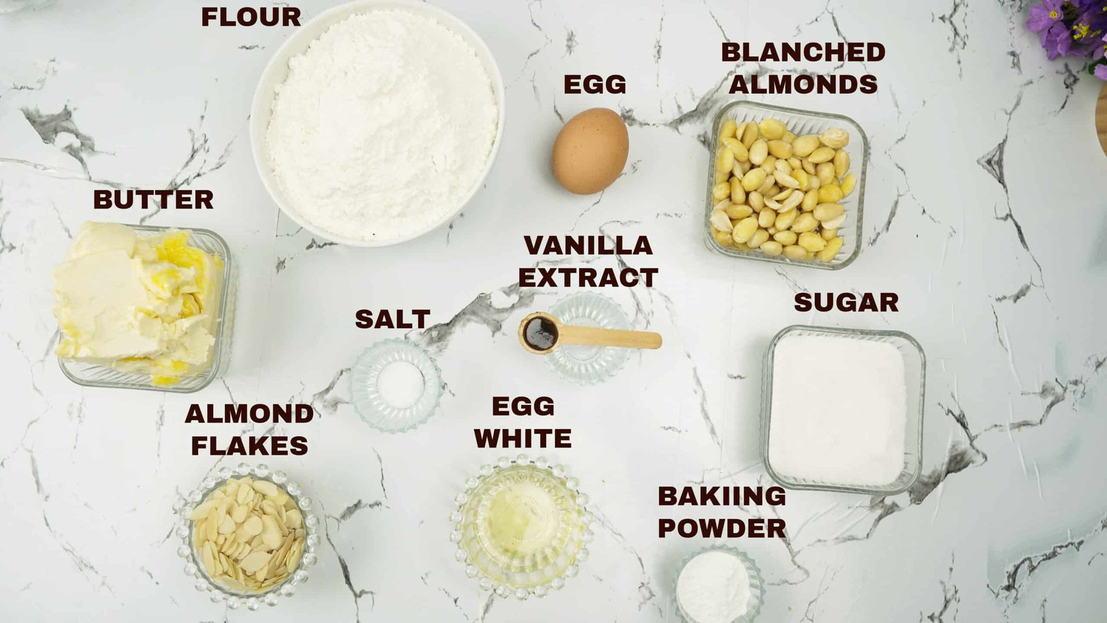 Butter, flour, sugar, eggs, almonds, and baking powder arranged on a counter