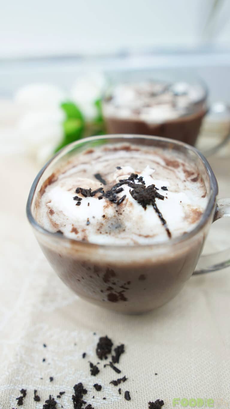 Glass mug of hot chocolate topped with whipped cream and chocolate flakes