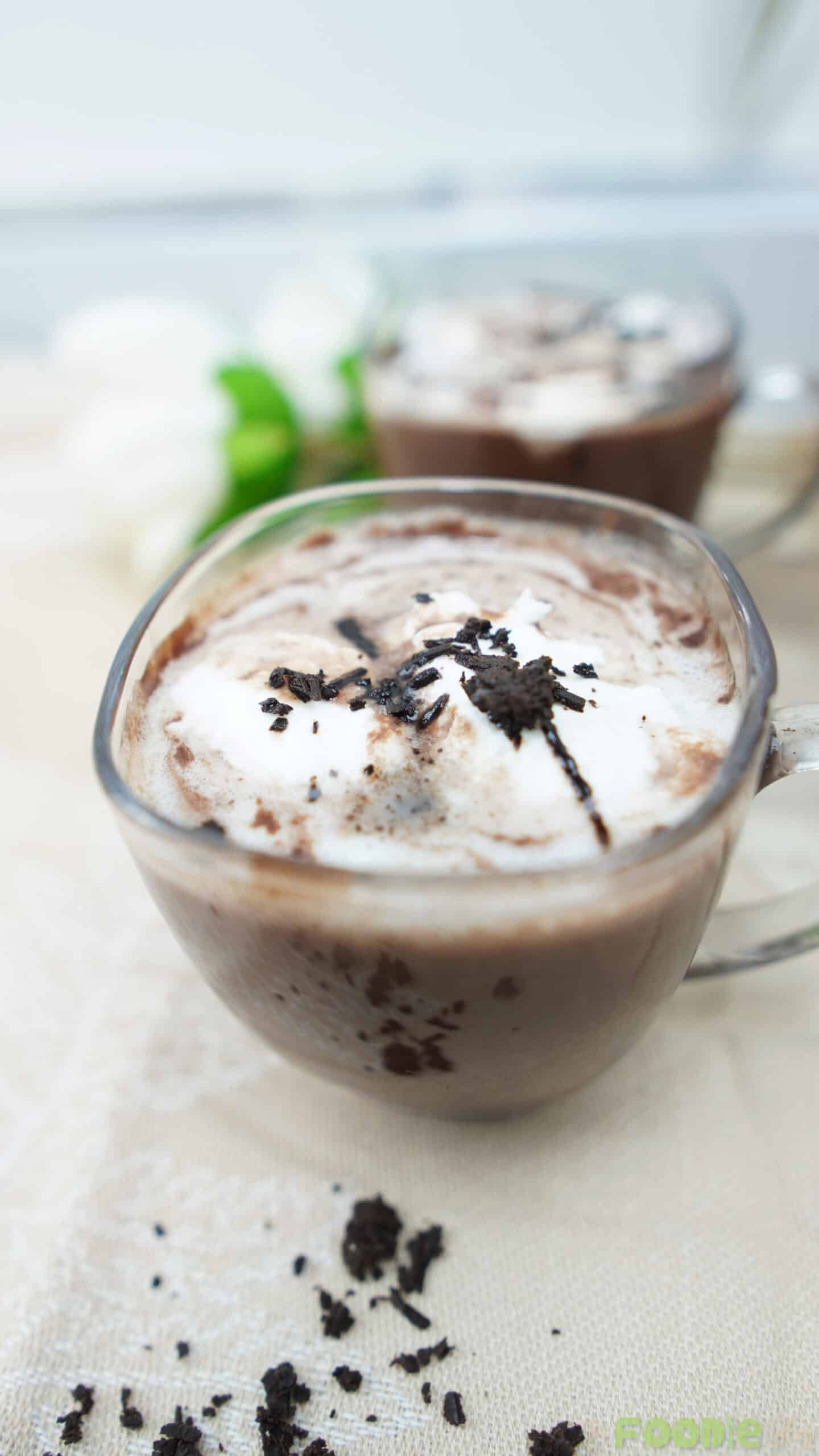 Glass mug of hot chocolate topped with whipped cream and chocolate flakes