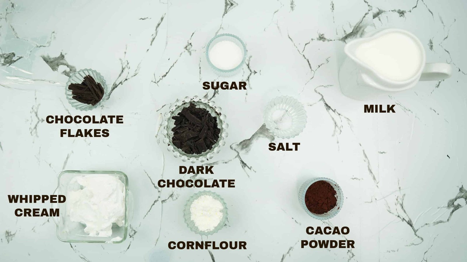 Milk, sugar, cocoa powder, cornstarch, dark chocolate, and whipped cream arranged on a countertop
