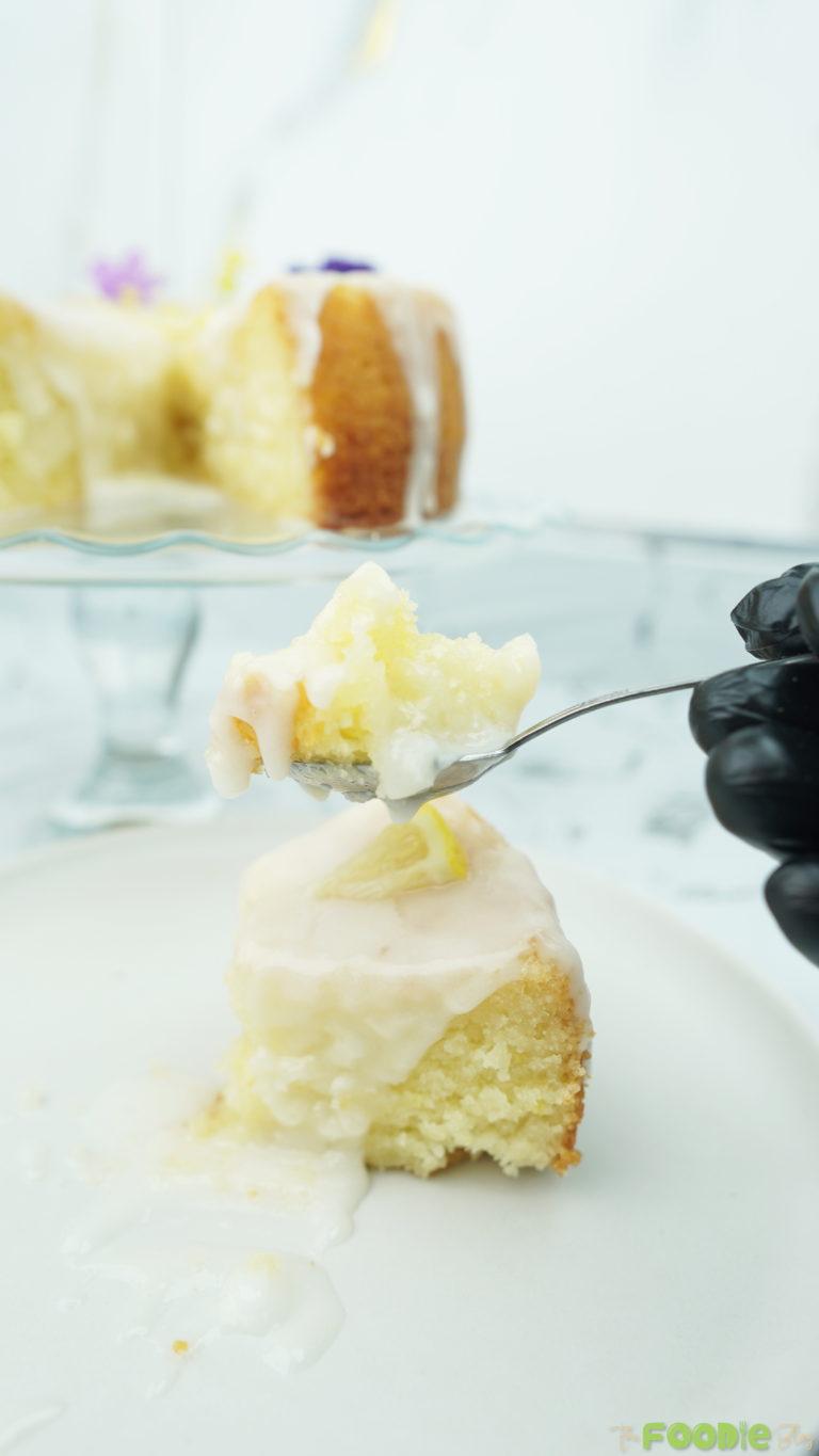 Spoonful of lemon cake with white glaze in front of a glazed cake on a stand