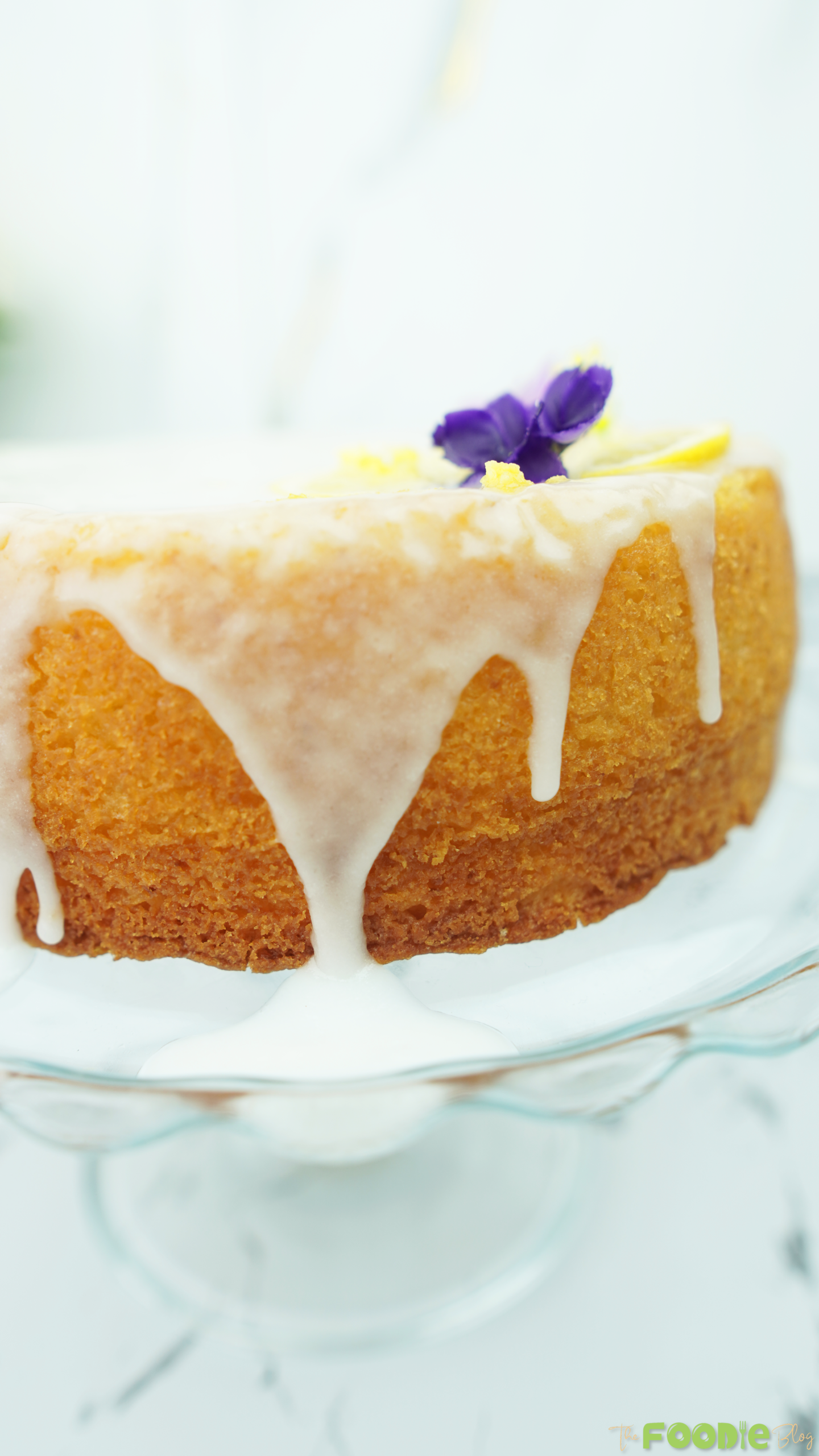 Close-up of lemon cake with lemon glaze dripping down the side on a glass cake stand