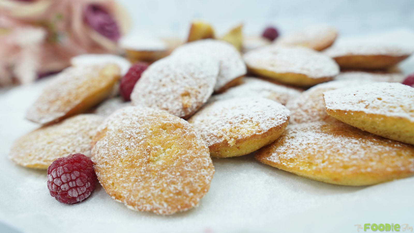 Close-up of madeleines dusted with powdered sugar with raspberries on a white plate