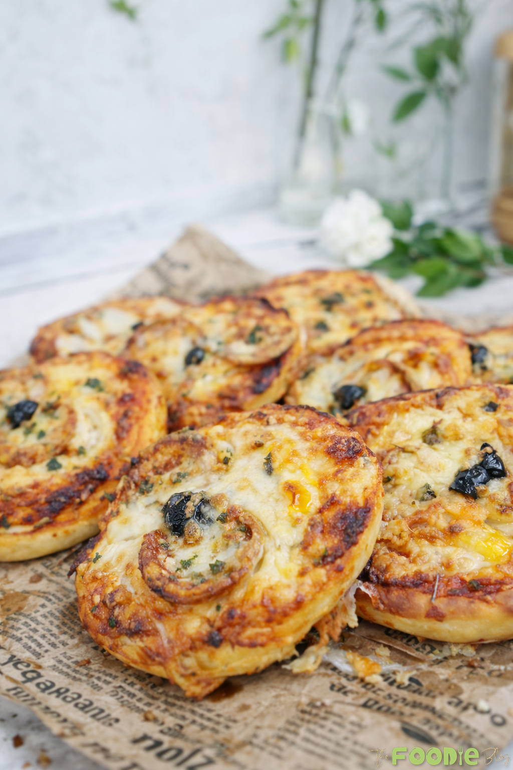 Close-up of mini pepperoni pizza with browned mozzarella, pepperoni slices, and black olive on newspaper-style paper