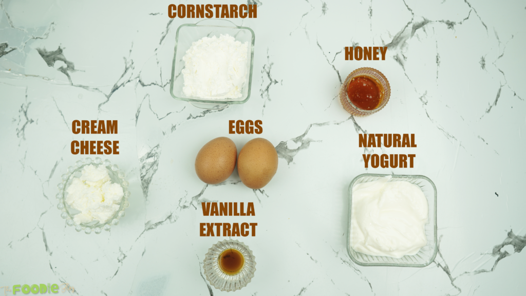 Eggs, yogurt, cornstarch, honey, vanilla, and cream cheese on a marble surface