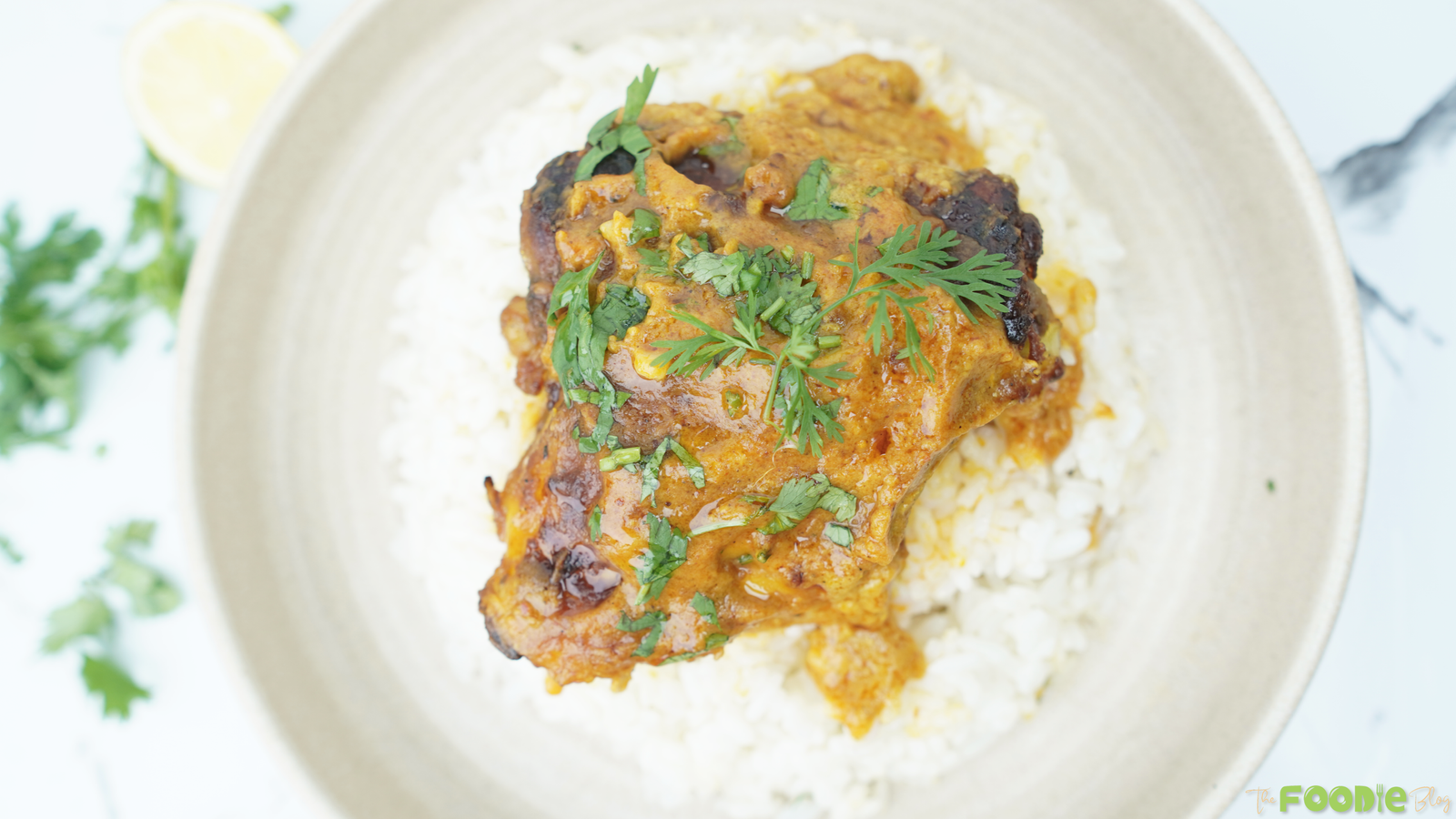 Butter chicken thigh served over basmati rice with fresh cilantro and a lemon wedge nearby
