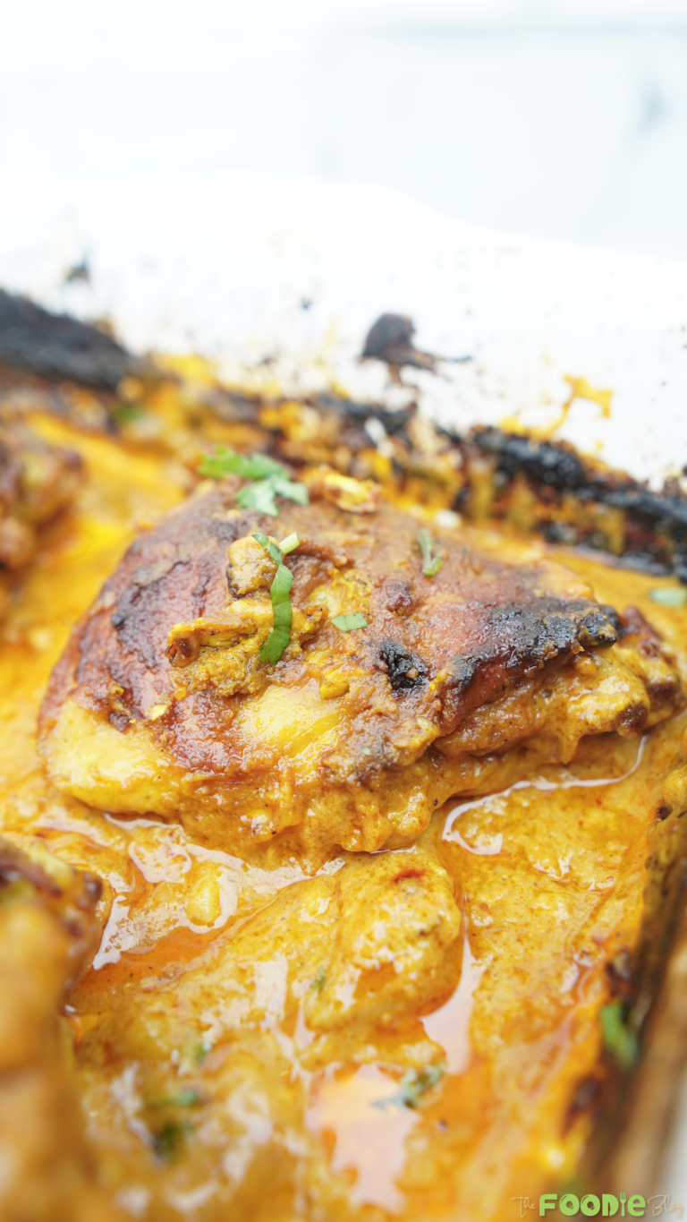 Close-up of baked butter chicken thighs in a creamy tomato sauce inside a baking dish