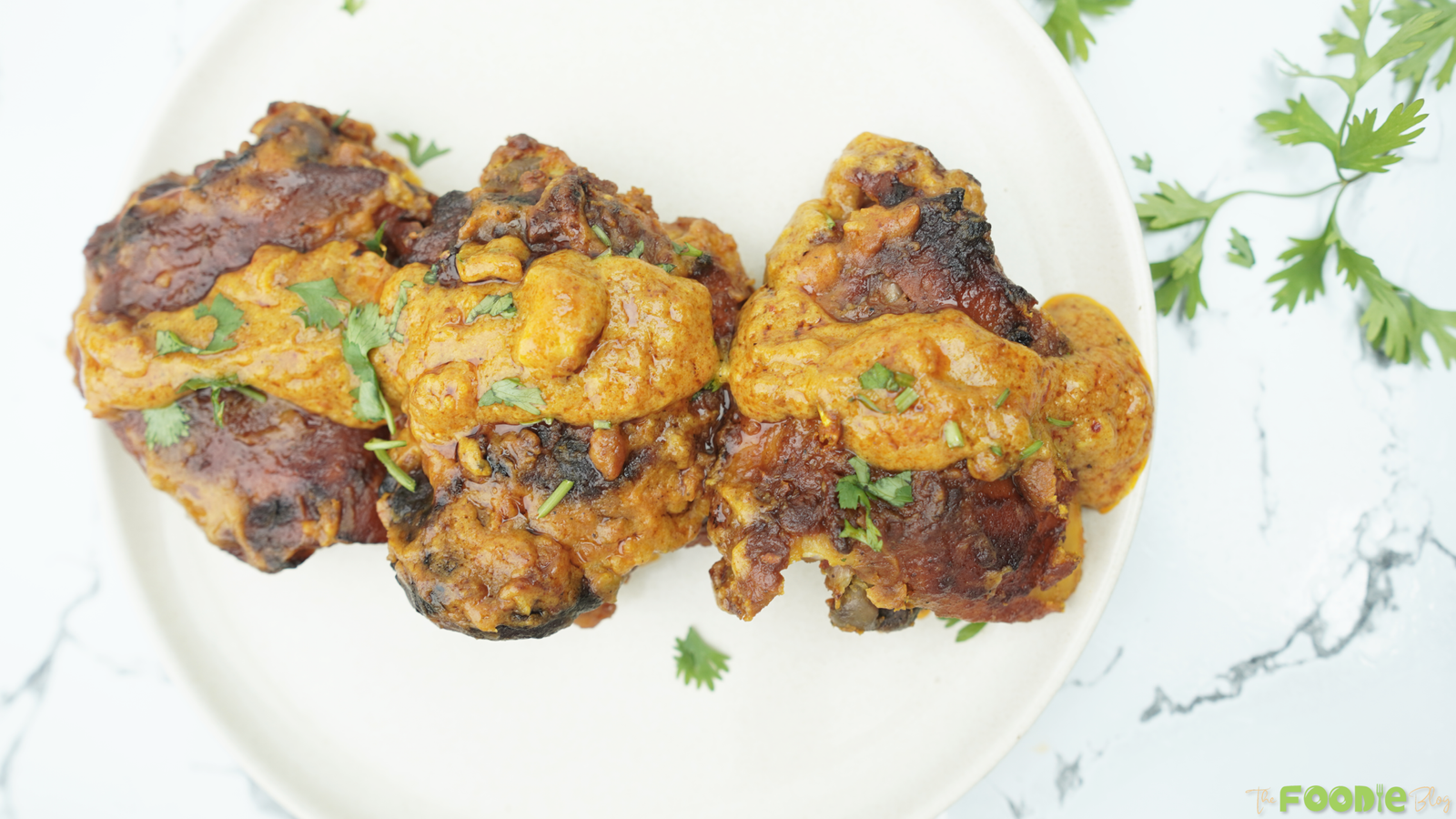 Baked butter chicken thighs coated in creamy tomato sauce on a white plate