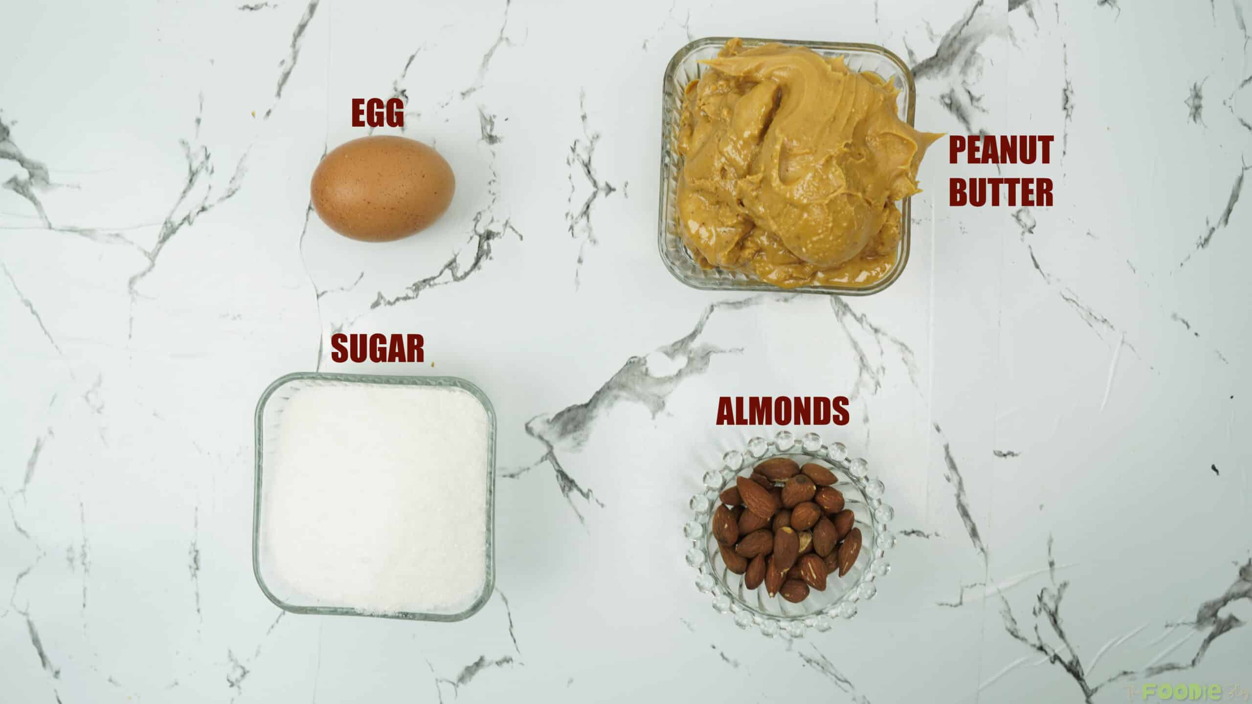 Peanut butter, sugar, egg, and almonds arranged on a counter for baking cookies