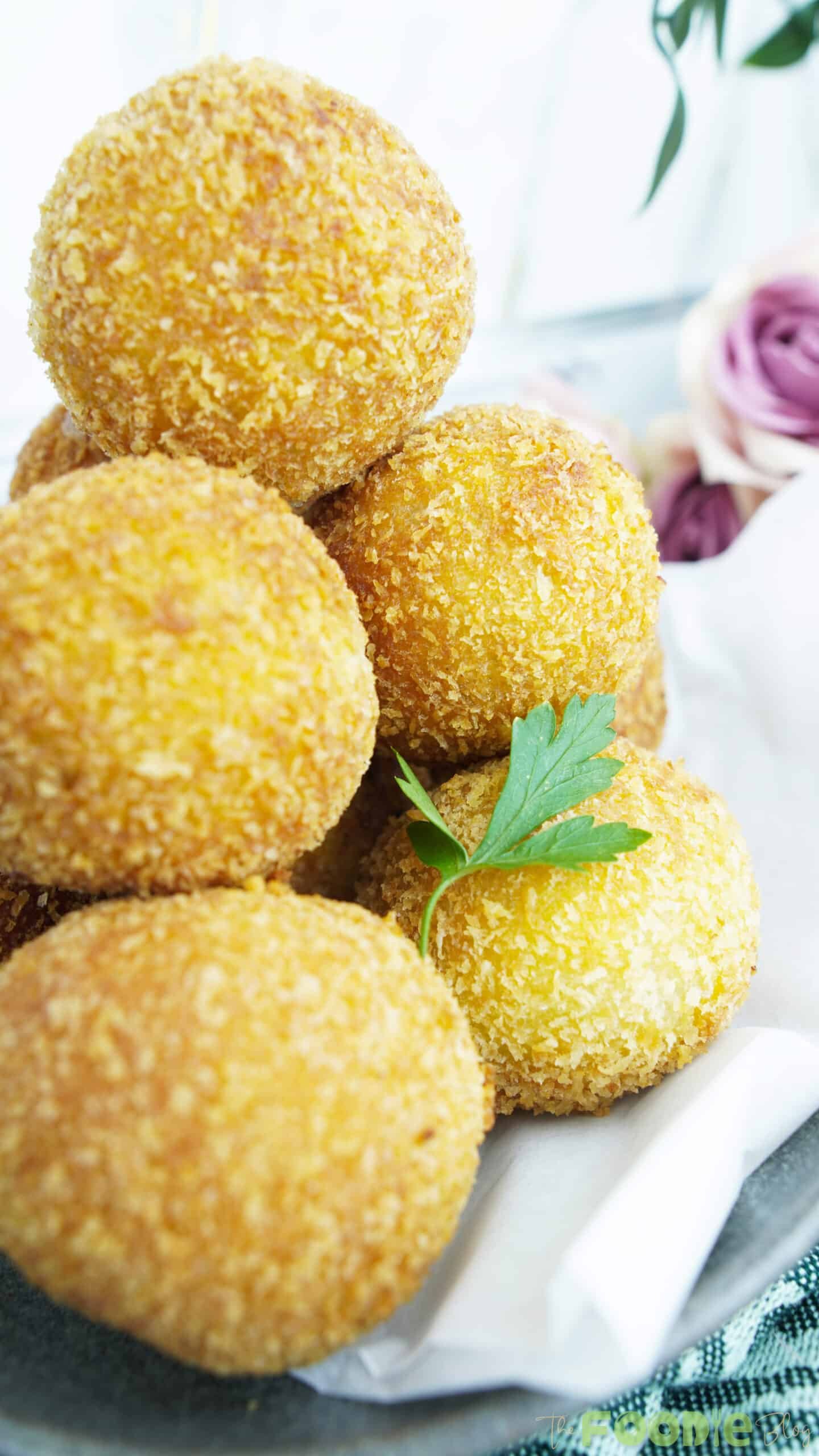 Golden potato cheese balls stacked on a plate with a parsley garnish