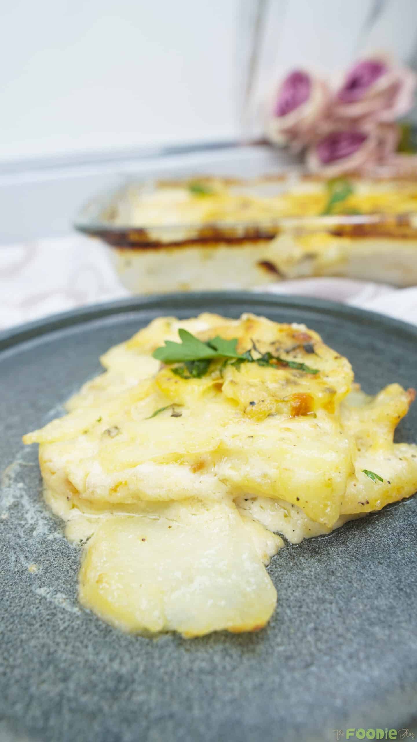 A serving of potatoes au gratin on a dark plate with creamy sauce and a browned top