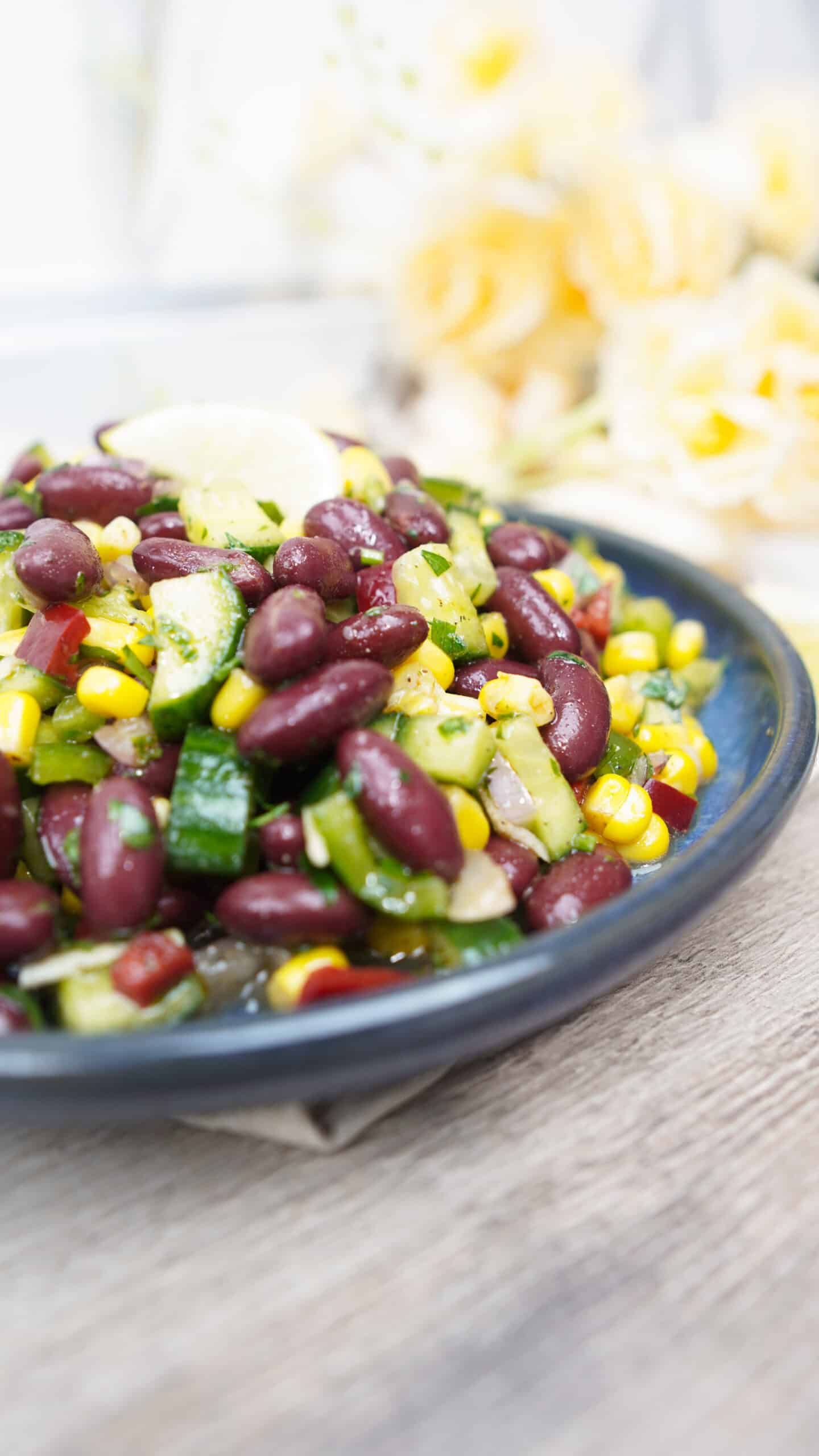 Side view of red bean salad in a blue bowl with cucumbers, corn, and peppers