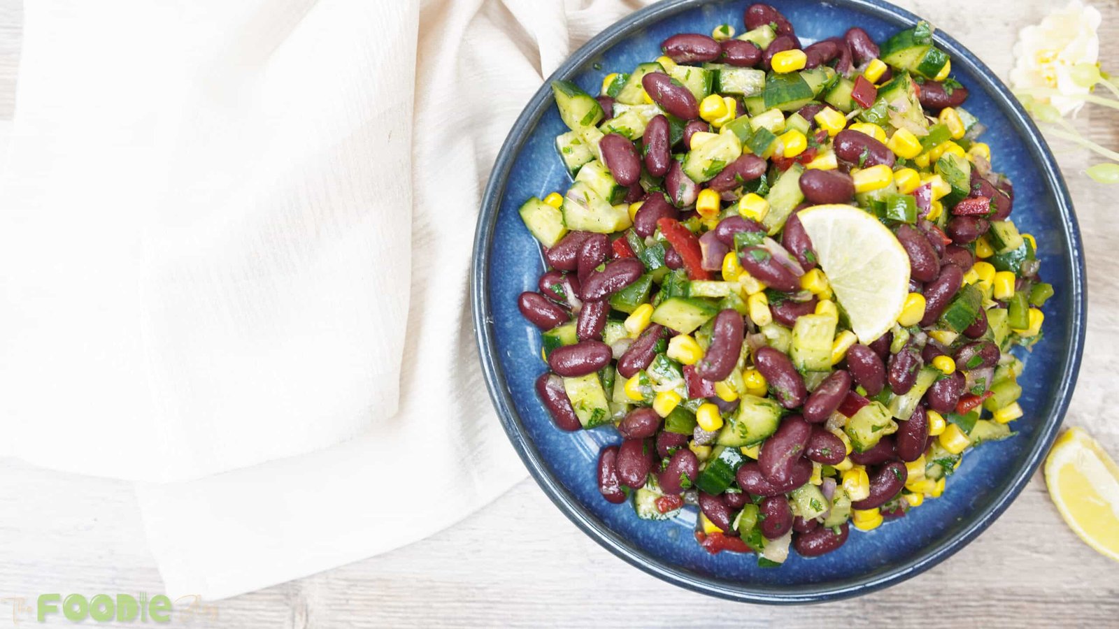 Red bean salad with cucumbers, corn, and peppers in a blue bowl with a lemon wedge