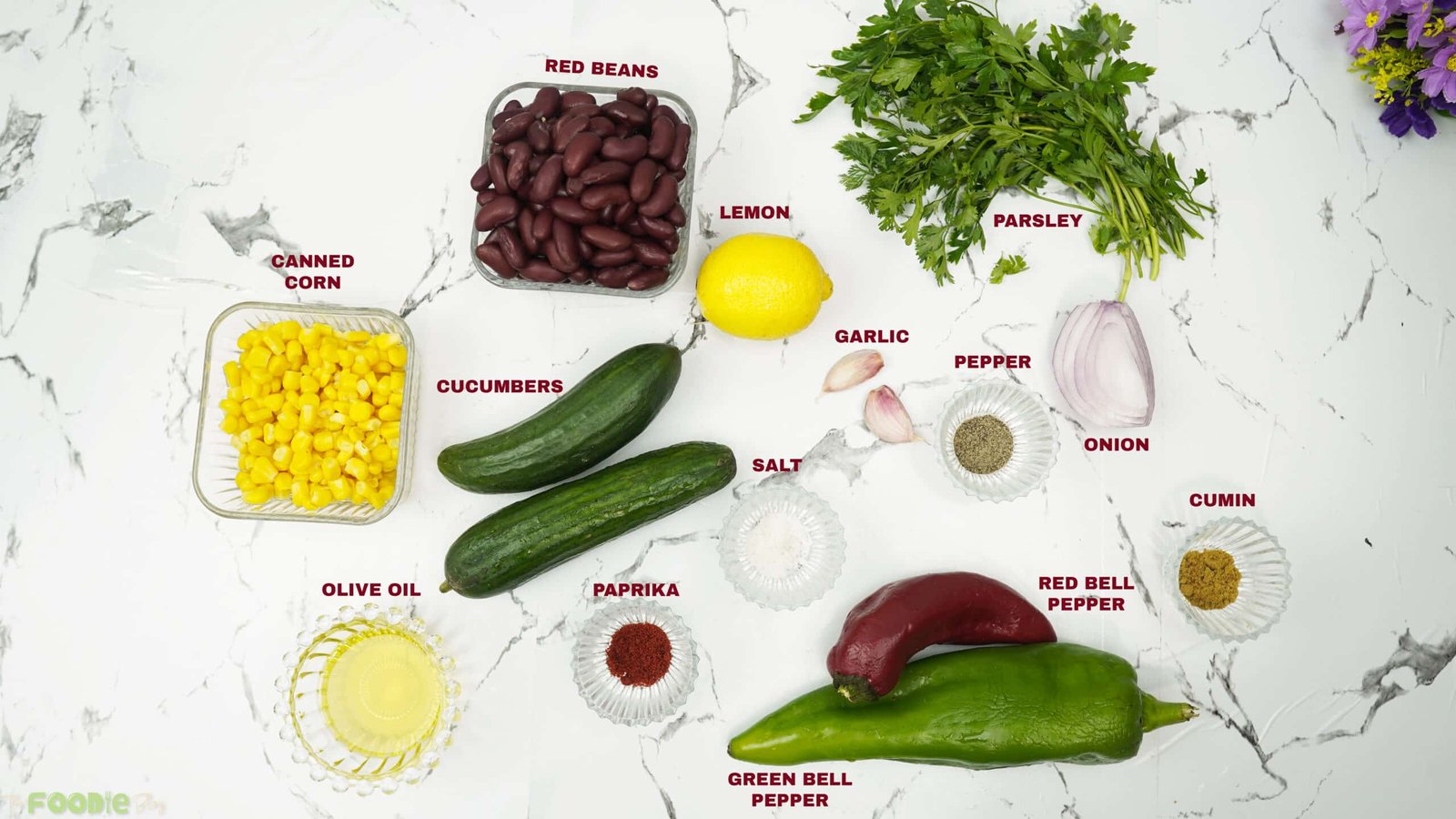Ingredients laid out for red bean salad including cucumbers, beans, corn, peppers, lemon, garlic, and spices