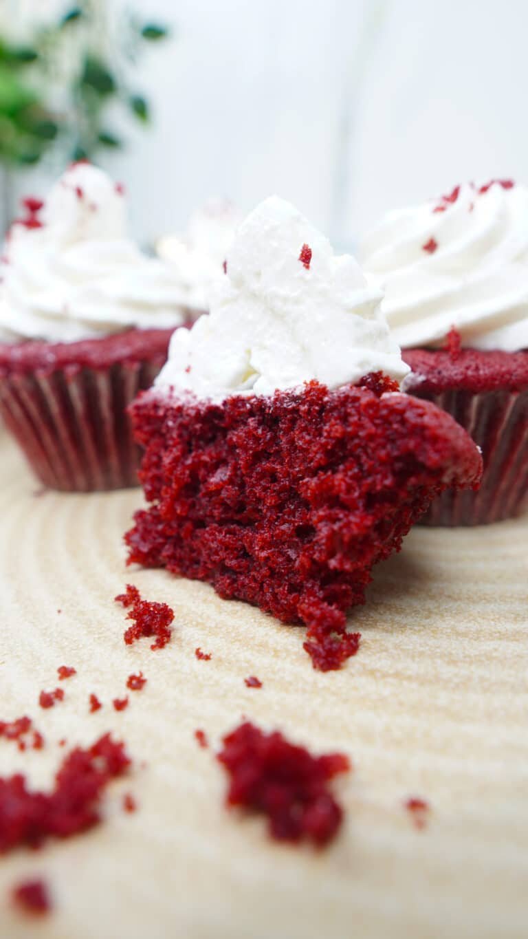 Bite-sized piece of red velvet cupcake with cream cheese frosting in the foreground