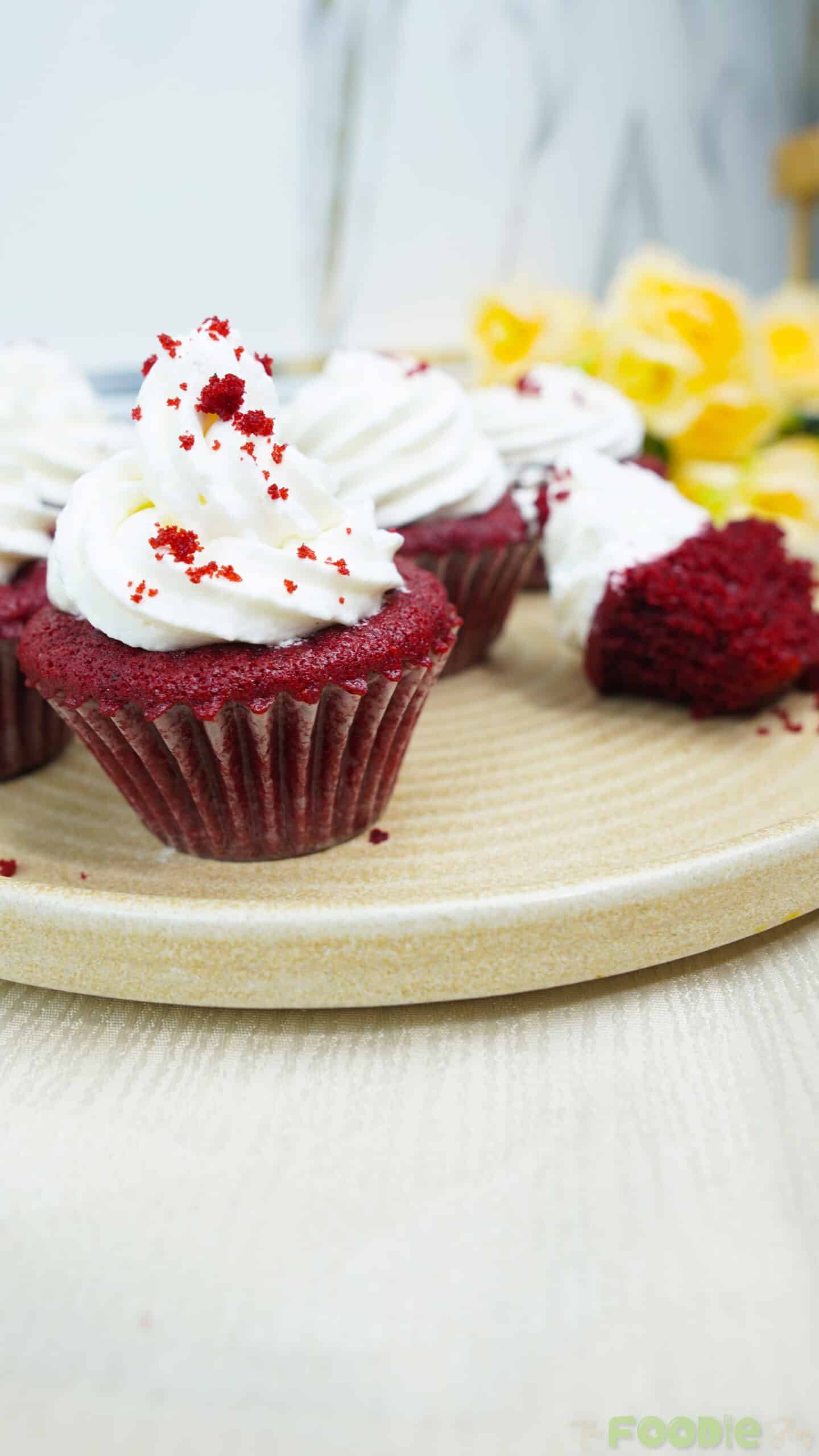 Red velvet cupcake topped with a swirl of cream cheese frosting on a plate