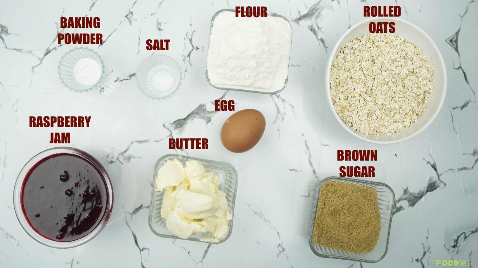 Flour, rolled oats, butter, brown sugar, egg, baking powder, salt, and raspberry jam on a counter