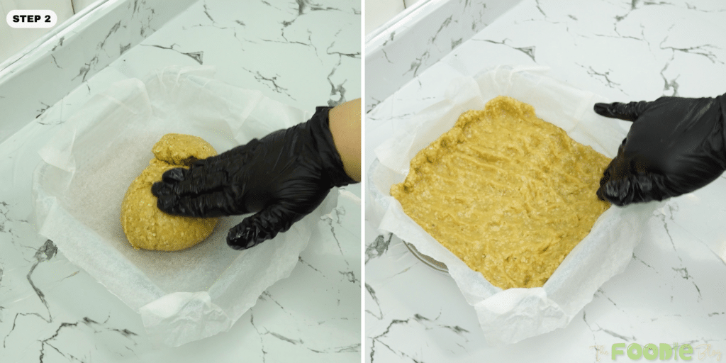 Hands pressing oat dough into a parchment-lined square baking pan