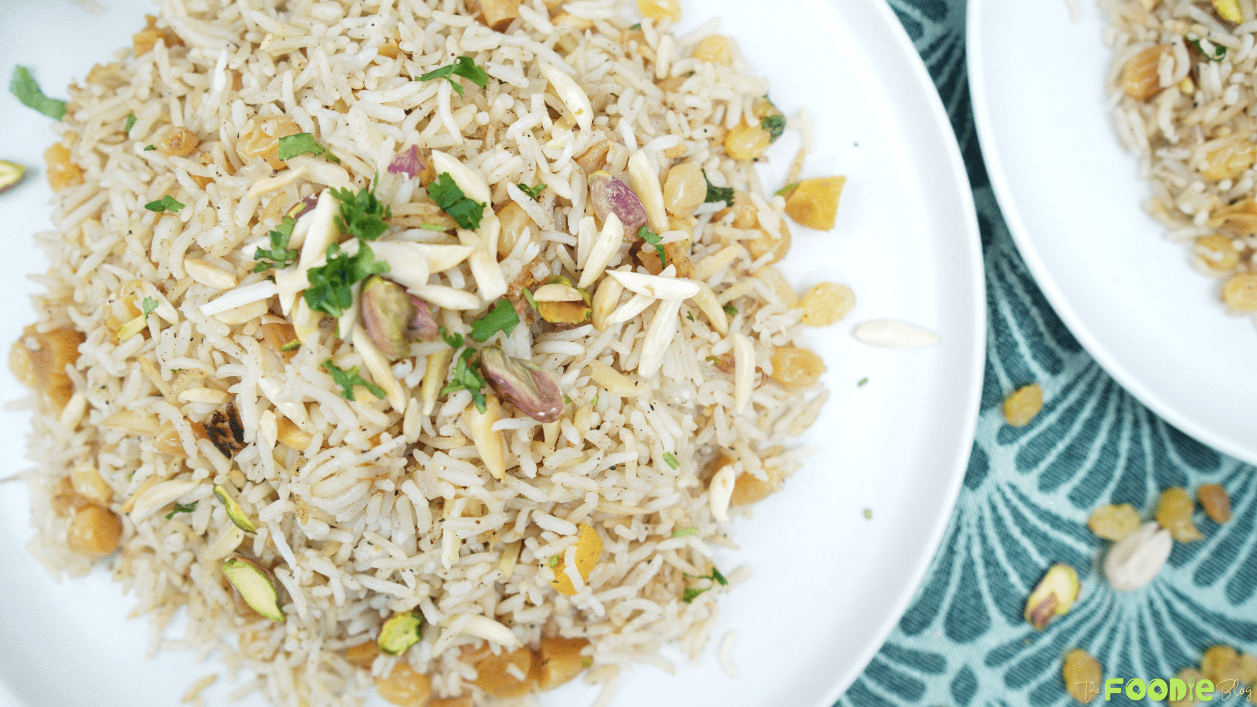 Overhead view of basmati rice pilaf topped with pistachios, slivered almonds, and parsley on a white plate