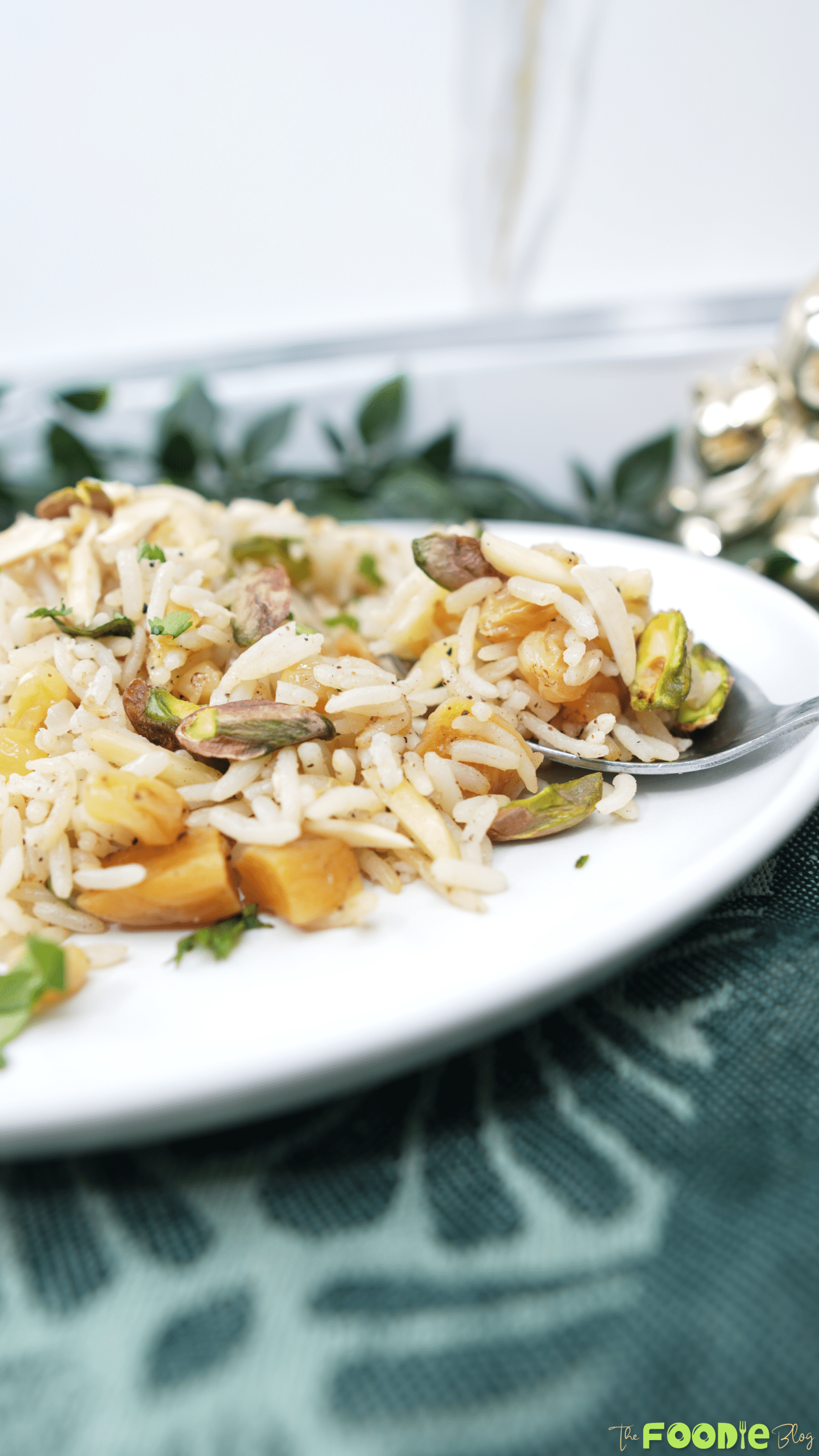 Spoon scooping fluffy rice pilaf with pistachios, almonds, raisins, and apricots from a white plate