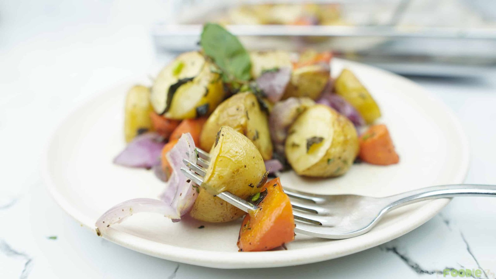 fork holding a piece of roasted potato and carrot over a plate of roasted vegetables