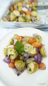 roasted vegetables on a white plate with potatoes, carrots, onion, and herbs