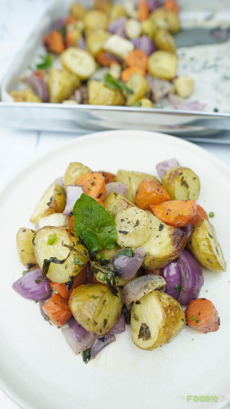 roasted vegetables on a white plate with potatoes, carrots, onion, and herbs