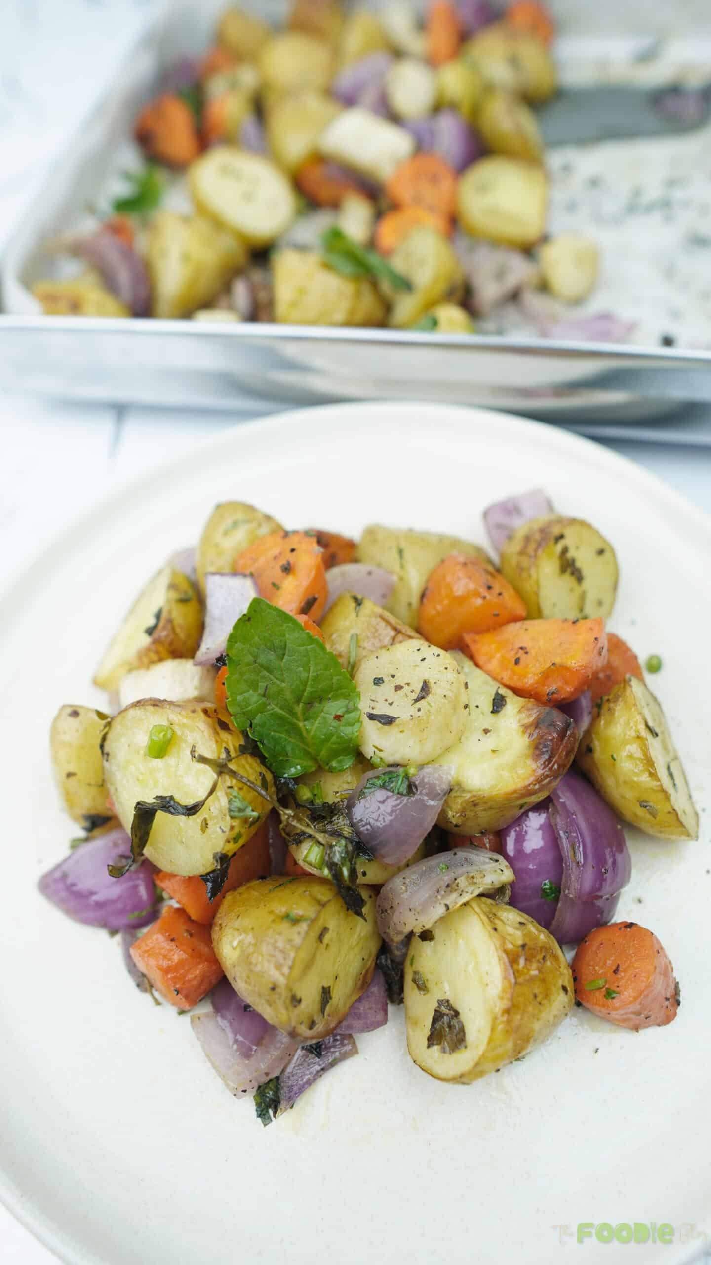 roasted vegetables on a white plate with potatoes, carrots, onion, and herbs