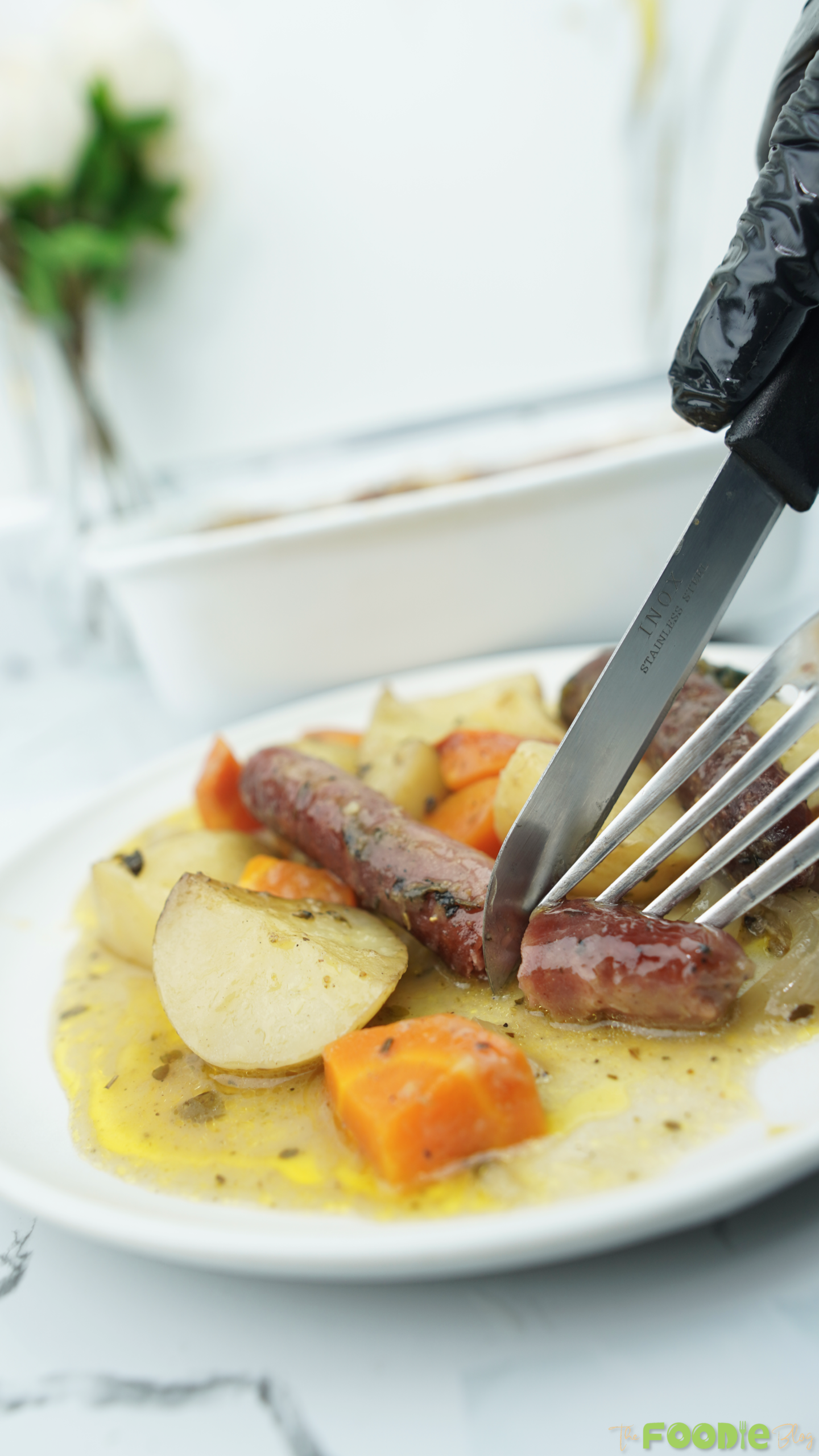Fork and knife cutting into a sausage on a plate with potatoes, carrots, and gravy