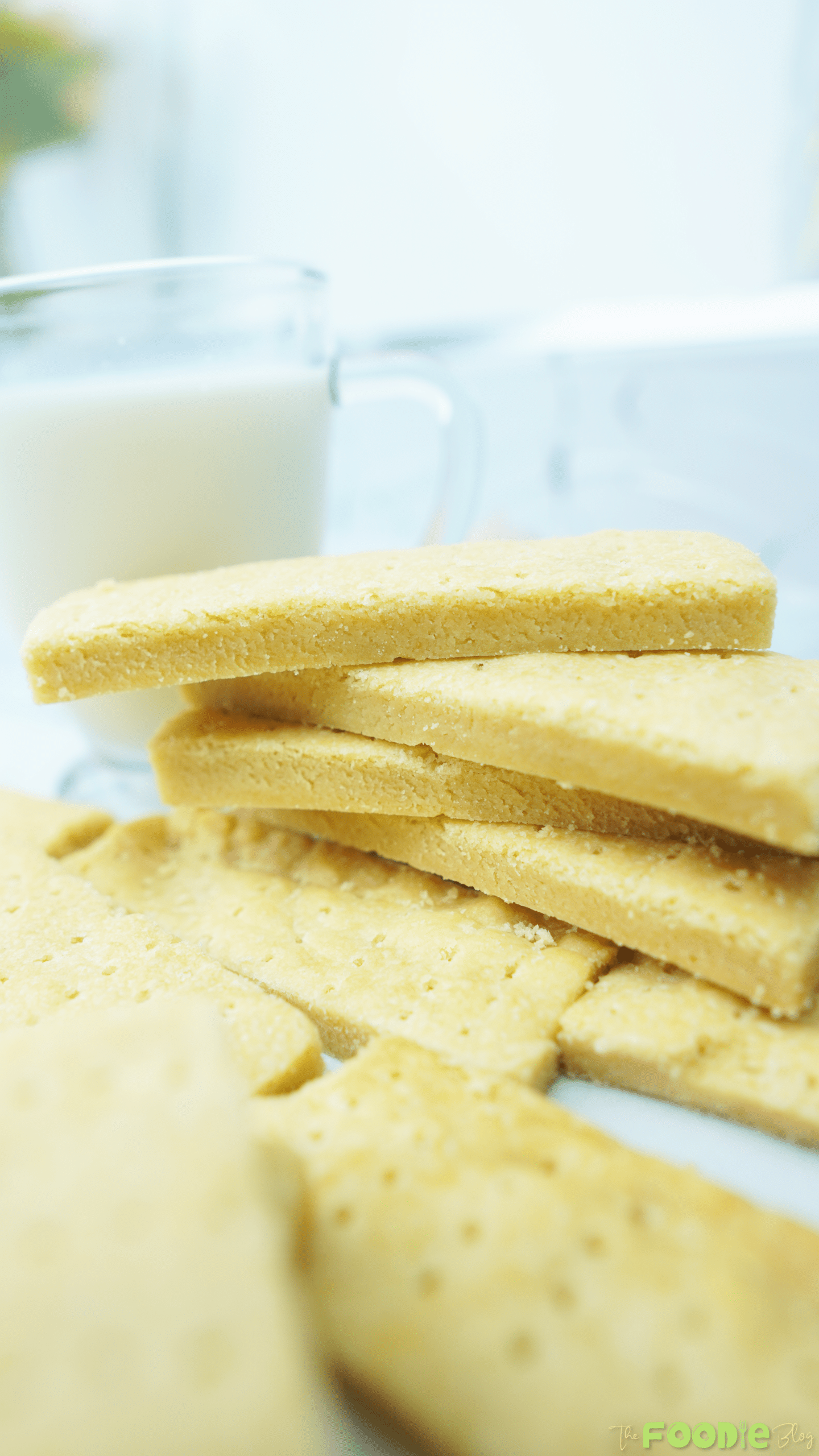 Stack of buttery shortbread cookie bars on a plate with a glass of milk in the background